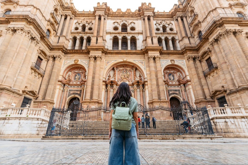 Woman with a green backpack admiring the facade of Málaga Cathedral, a historic Renaissance landmark in Andalusia, Spain.