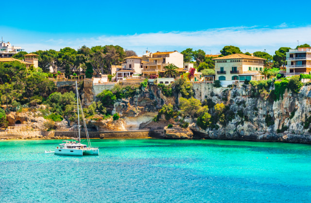 Beautiful view of the coast of mallorca where we can see the blue water, a sailboat and the beautiful local buildings.