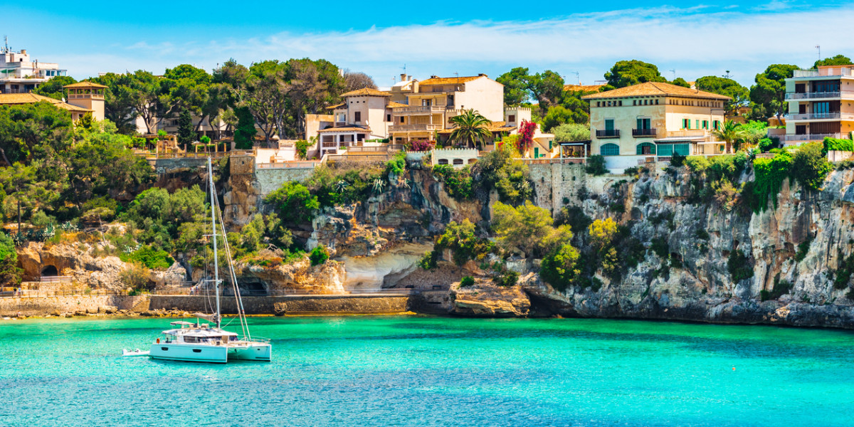 Beautiful view of the coast of mallorca where we can see the blue water, a sailboat and the beautiful local buildings.