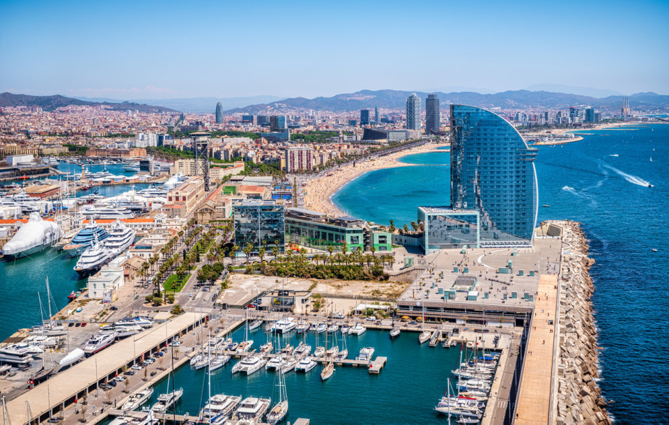 Aerial view of Barcelona’s waterfront, featuring Port Olímpic, the beach and the city skyline along the Mediterranean Sea, one of the most attractive areas for coastal living and buying a second home in Spain.