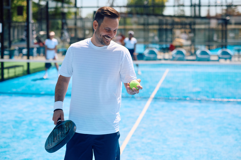 Padel player with a happy smile before serving and returning to play on a beautiful sunny day.
