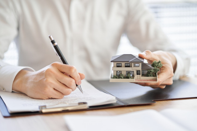 A person registering a property, thoughtfully considering a house, with a form and a house icon visible on the screen.