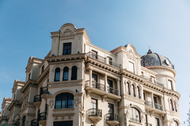 Facade of a luxury building in Madrid under a clear blue sky, featuring traditional Spanish architecture with ornate details and elegant balconies.