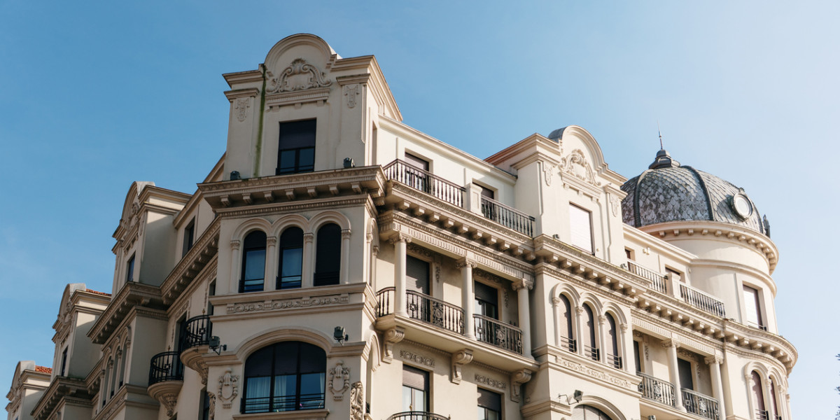 Facade of a luxury building in Madrid under a clear blue sky, featuring traditional Spanish architecture with ornate details and elegant balconies.