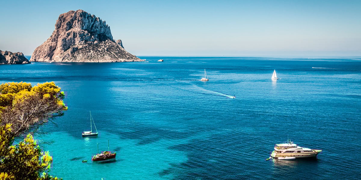 Panoramic view of Ibiza with turquoise-blue sea, anchored boats, and the island's characteristic rocky landscape