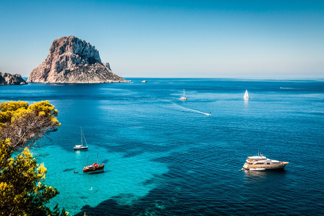 Panoramic view of Ibiza with turquoise-blue sea, anchored boats, and the island's characteristic rocky landscape