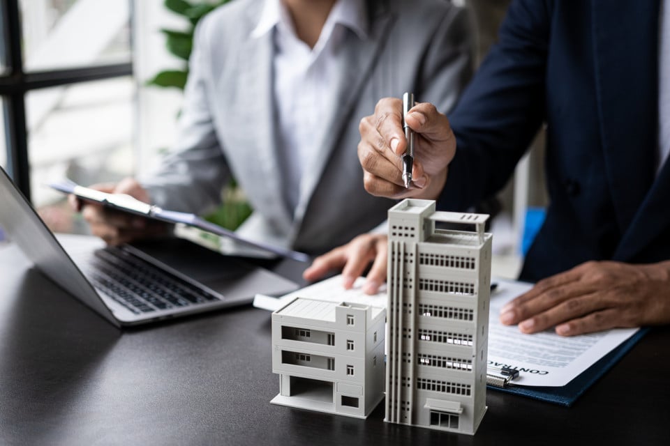 Two people engaged in a discussion about real estate taxes, sitting at a table with documents and a calculator, appearing focused and professional.