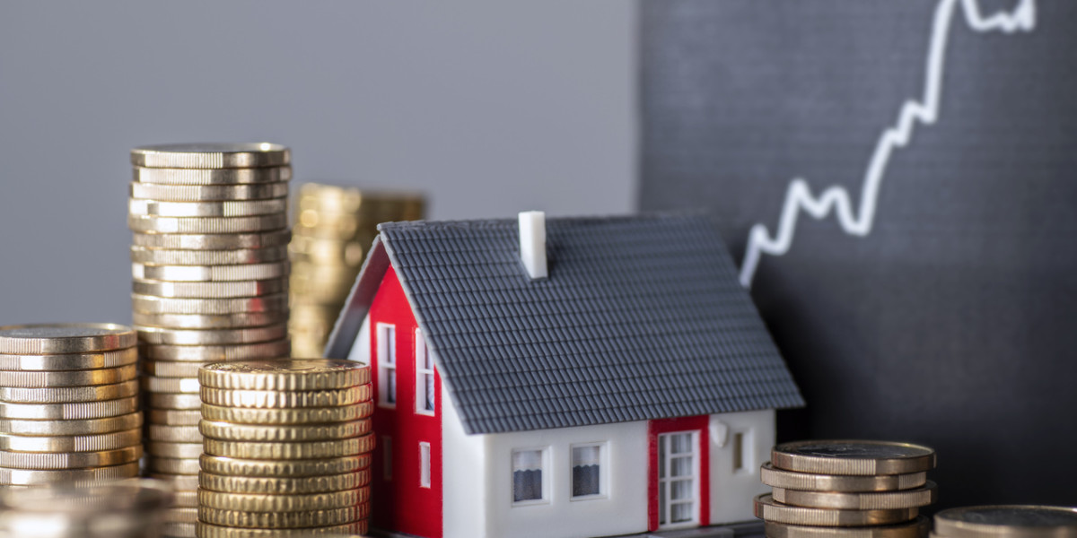 Stacks of coins beside a miniature house representing property valuation and real estate investment in Spain.