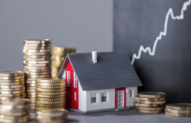 Stacks of coins beside a miniature house representing property valuation and real estate investment in Spain.