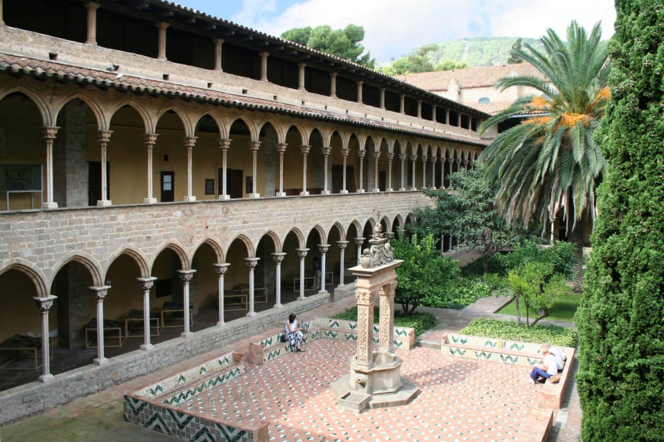 Inner courtyard of the Monastery of Pedralbes in Barcelona, featuring Gothic arches, a central fountain, and lush Mediterranean gardens.