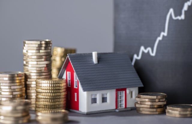 Stacks of coins beside a miniature house representing property valuation and real estate investment in Spain.