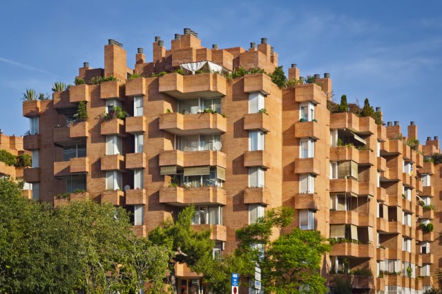 Modern residential building in Barcelona with distinctive terraced brick balconies and lush greenery.
