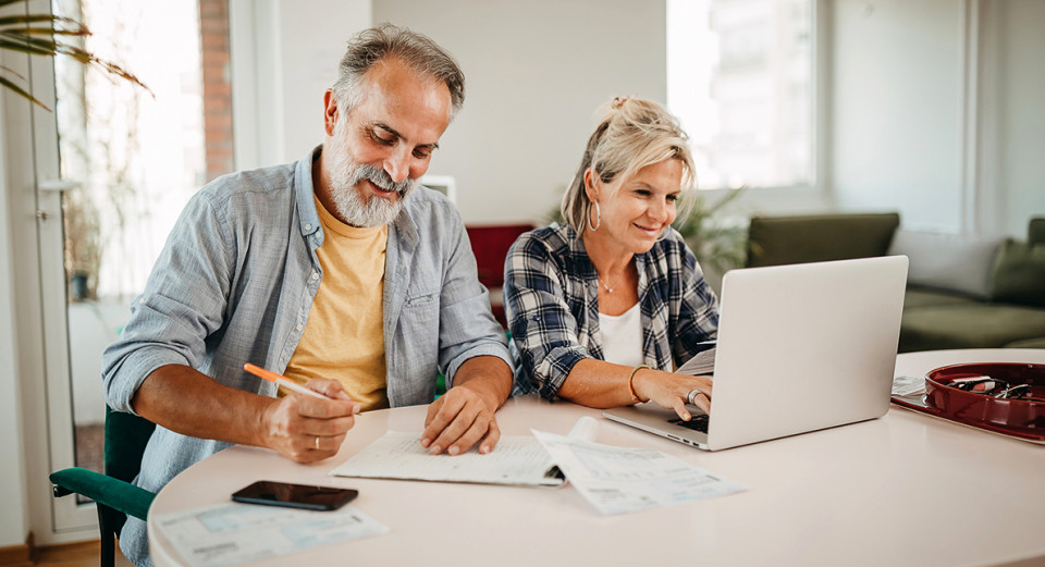 Adult couple contemplating mortgage and post home purchase costs sitting at the living room table at the computer.