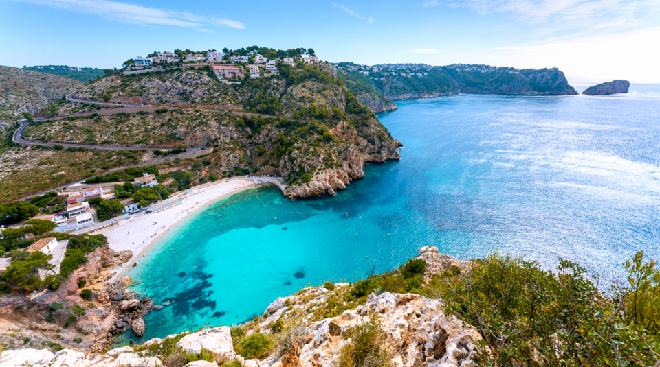 Javea beach aerial view where you can see the blue water and the houses embedded in the mountain.